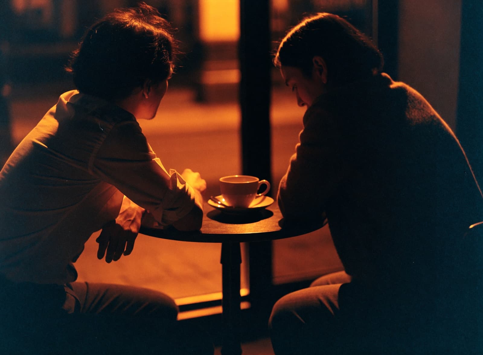 Two people talking over coffee at a warm, low-lit table